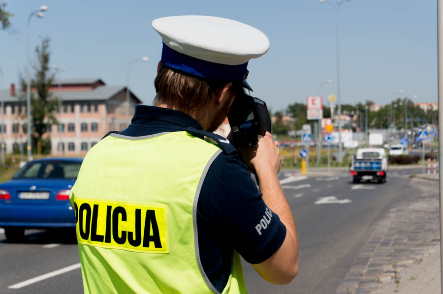 zdjęcie przedstawia policjanta drogówki z radarowym miernikiem prędkości w trakcie dokonywania pomiaru