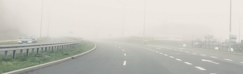 droga w mgle i samochód jadący z włączonymi światłami dziennymi