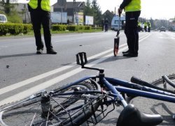 zdjęcie poglądowe - leżący rower na ulicy po wypadku, w tle policjanci drogówki