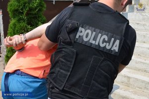 zdjęcie poglądowe - policjant prowadzi zatrzymanego mężczyznę z kajdankami na rękach