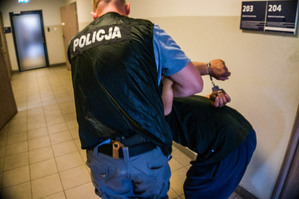 zdjęcie poglądowe z archiwum policji - policjant prowadzi zatrzymanego korytarzem