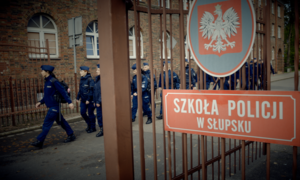 zdjęcie z filmu, brama wejściowa do szkoły policji w słupsku, z terenu uczelni wychodzą umundurowani policjanci - słuchacze szkoły