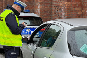 zdjęcie przedstawiające kontrolę pojazdu - policjant z drogówki stojący przy srebrnym samochodzie osobowym