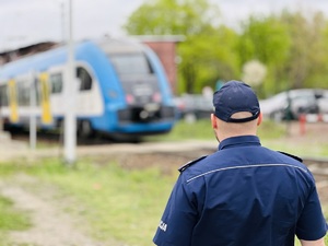 zdjęcie przedstawia policjanta stojącego przy torach po których jedzie pociąg pasażerski