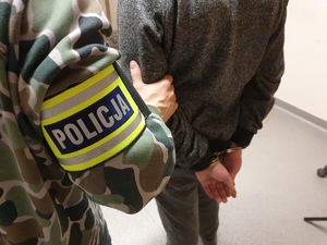 zdjęcie ilustracyjne - policjant kryminalny prowadzi zatrzymanego w kajdankach