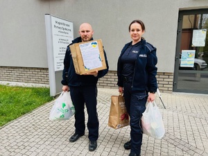 zdjęcie przedstawia policjanta i policjantkę z częścią darów stojących przed siedzibą rudzkiego ośrodka pomocy społecznej