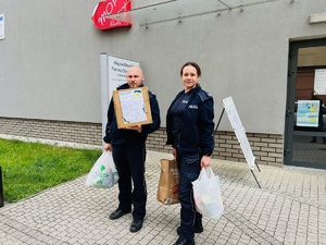 zdjęcie przedstawia policjanta i policjantkę z częścią darów stojących przed siedzibą rudzkiego ośrodka pomocy społecznej